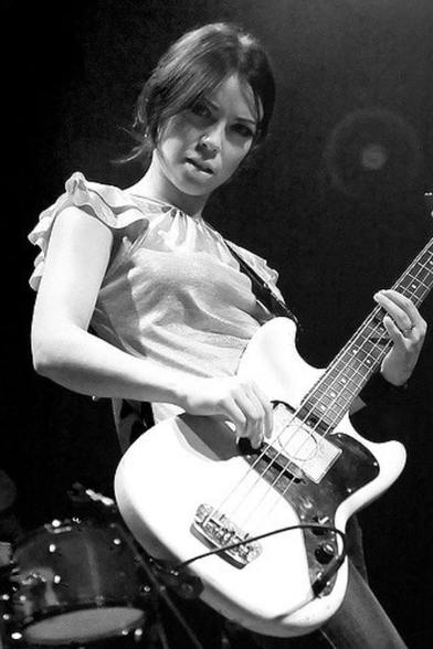 A monochrome image of Emm Gryner, a young Filipina-Irish Canadian woman, playing bass guitar. She's got an appropriately rocking facial expression and pose.