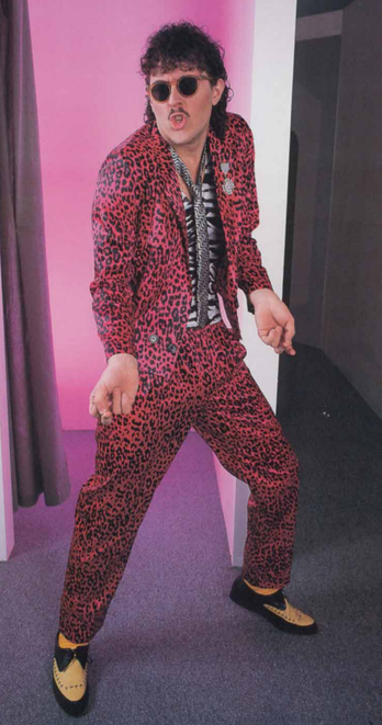 Al Yankovic dressed in a red leopard-skin suit over a zebra-striped shirt with a skinny tie. He's wearing dark sunglasses and his shoulder-length hair is in tight curls.