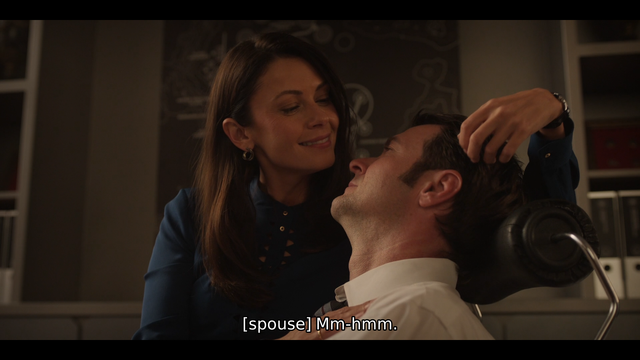 A dark-haired woman stroking the hair of her husband. The closed captioning reads "[spouse] Mm-hmm."